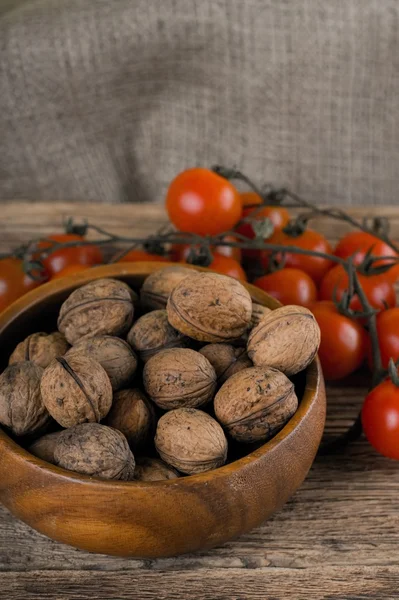 Wooden bowl full of walnuts and branch of tomatoes — 图库照片