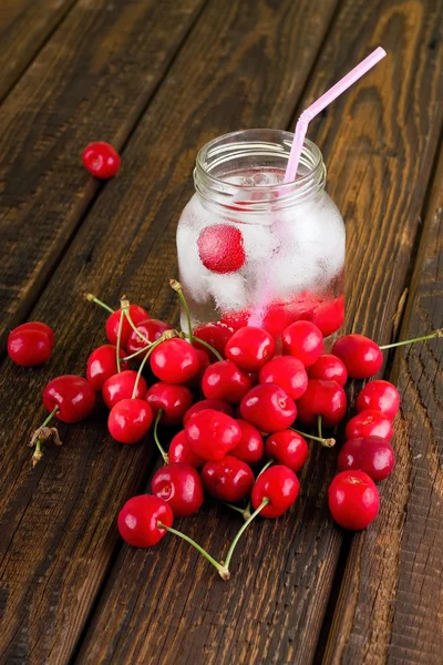 Cold drink in a jar with pink straw among several cherries