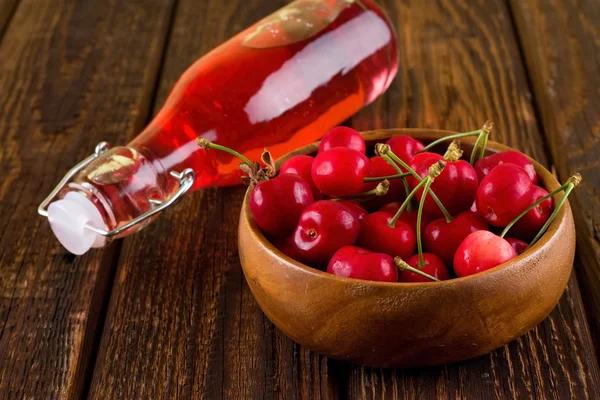 Full bowl with cherries in front of bottle with red drink — Zdjęcie stockowe