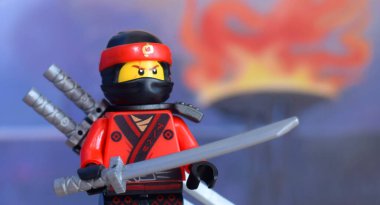 Lego minifügure Kai 'nin ateşli arka planda kılıç taşıyan kırmızı ninjasının editoryal çizimi.