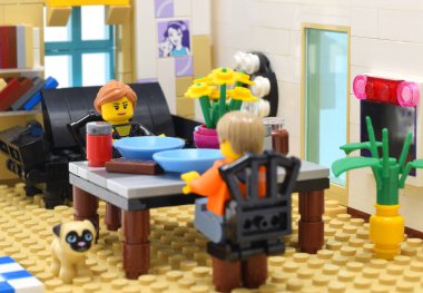 Lego minyatürleri masada çiçeklerle yemek yiyorlar. Yaşam tarzının editoryal illüstrasyon görüntüsü. Stüdyo çekimi. 