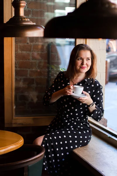 モダンなロフトカフェバーの窓の近くに座っている間 美しい女性の肖像画はコーヒーを飲んでいます 離れて見て夢の女性の肖像画 — ストック写真