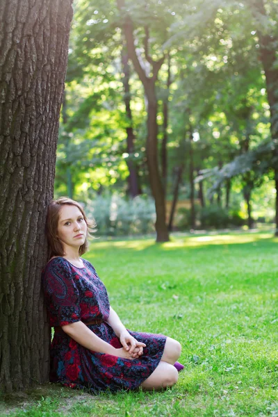 Bir ağacın altında oturan üzgün genç kadın — Stok fotoğraf