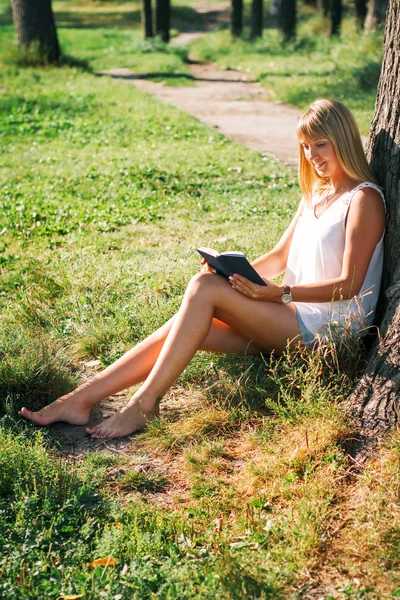 Jonge vrouw zitten in het park en het lezen van een boek — Stockfoto