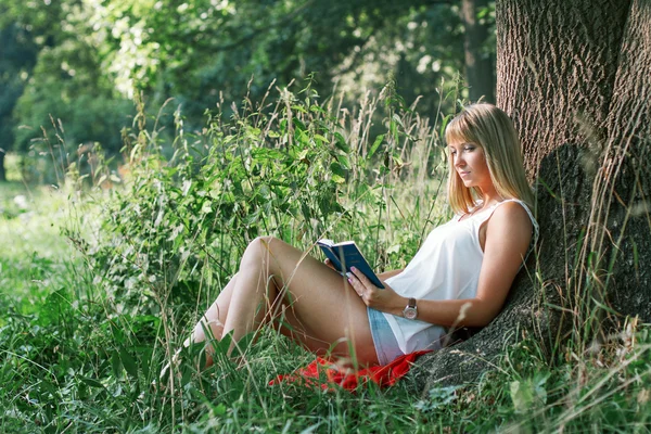 Jonge vrouw onder een boom zitten en lezen van een boek — Stockfoto