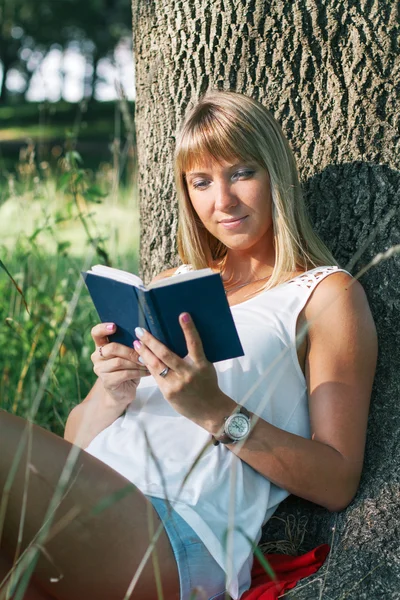 Ung kvinna sitter i parken och läser en bok — Stockfoto