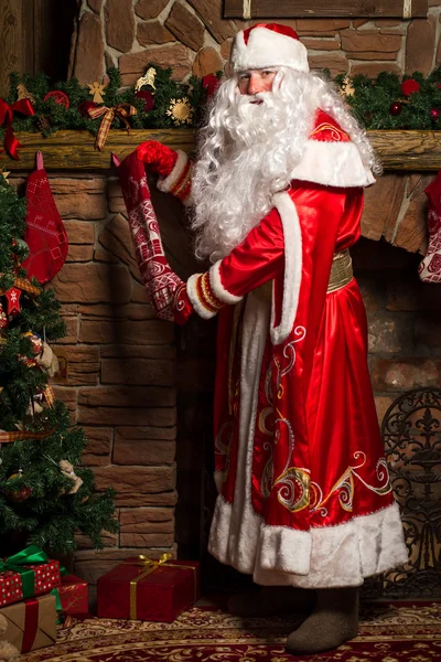 Санта Клаус кладет подарки в рождественские чулки у камина — стоковое фото
