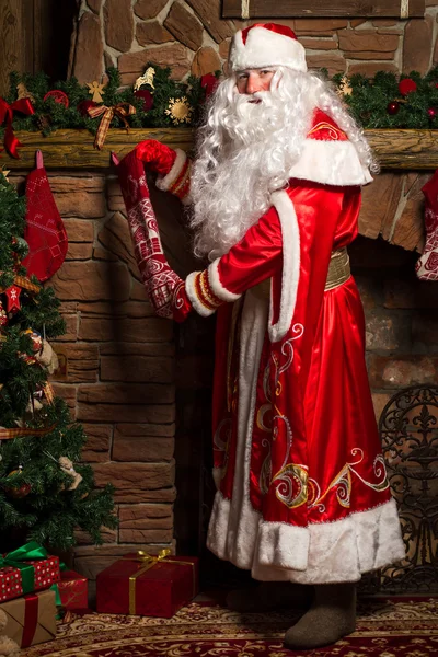 Santa Claus geschenken aanbrengend Kerstmis kousen bij open haard — Stockfoto