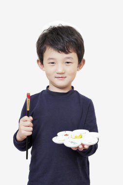 Asyalı çocuk çocuk boyama fırça ve renk paleti ile tutar