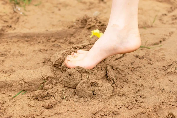 In summer, the child plays on the beach, runs barefoot on the sand. Sea tour. Childrens feet in the sand. Entertainment in the fresh air..