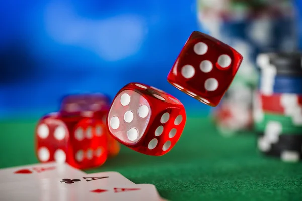 Red dice rotates in the air, casino chips, cards on green felt