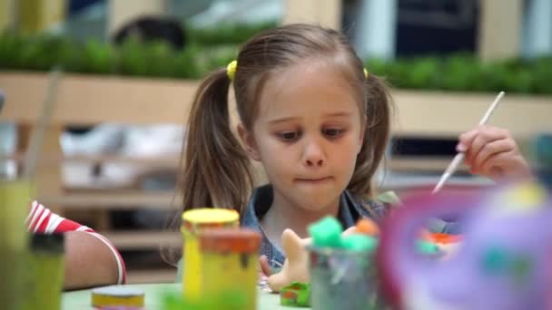 Маленька дівчинка малює керамічного кота за столом — стокове відео