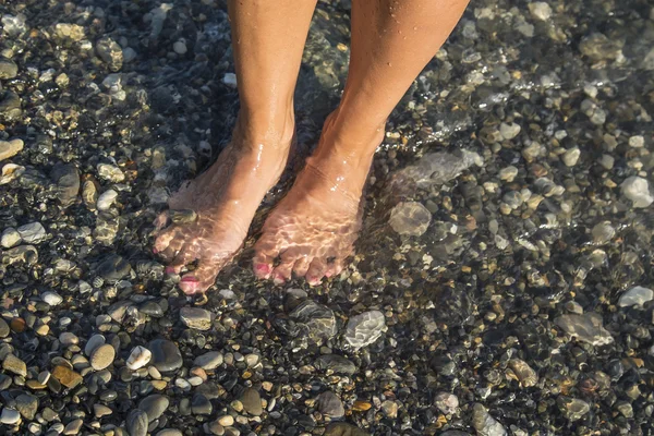 Jeune et belle femme pieds nus avec des ongles peints en rouge debout sur une plage sous les vagues . — Photo