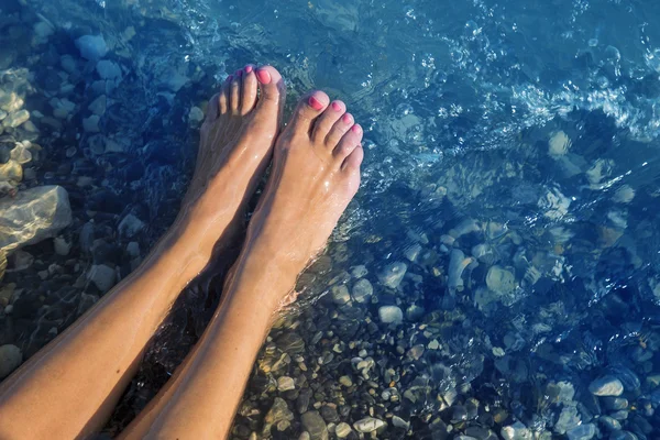 Jonge en mooie vrouwelijke blote voeten met rode gelakte nagels permanent op een strand onder de golven. — Stockfoto