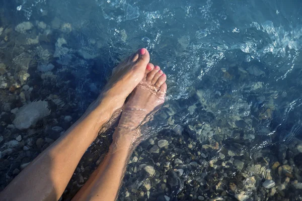 Νέοι και όμορφη γυναικεία πόδια με κόκκινα βαμμένα νύχια σε μια παραλία κάτω από τα κύματα. Εικόνα Αρχείου