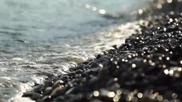 Gros plan sur les vagues du film et les chutes qui rebondissent sur une plage de galets avec une faible profondeur de champ . — Video
