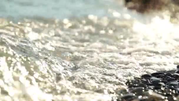 Close-up movie waves and drops lapping agains a pebble beach with shallow depth of field. — Stock Video