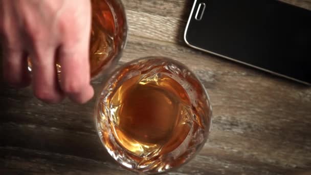Glasses of whiskey with ice on wooden table. — Stock Video
