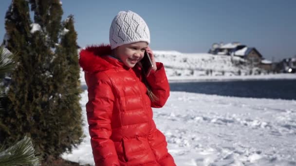 Маленькая девочка в красной куртке разговаривает по телефону — стоковое видео