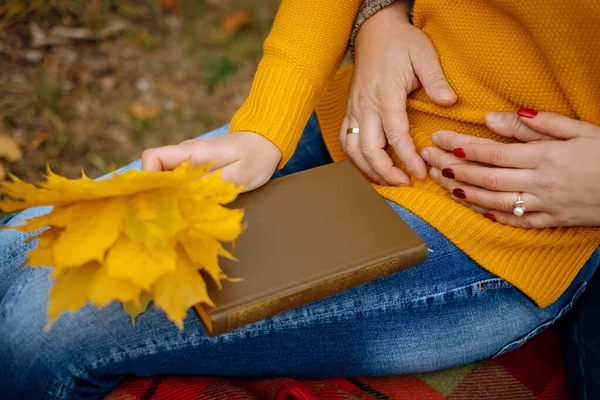Yıllanmış evli çift sonbaharda ormanda bir kitapla tatile çıkıyor. Kitap, sarı yapraklar, eller birbirine yakın çekim. Romantik.