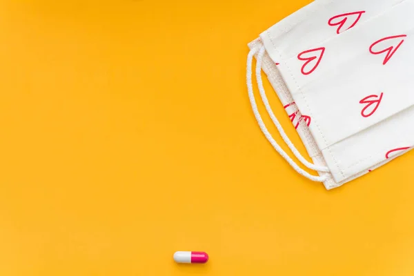 Kırmızı kapsül ve parlak sarı arka planda kırmızı desenli beyaz bir maske. Hastalık ilacı. Coronavirus virüsü hastalığından alınan ilaçlar ve sağlık için vitaminler. Kapatın. Boşluğu kopyala.