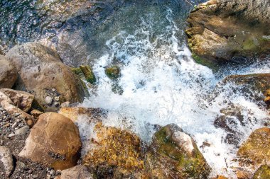 Dağ nehrinin akıntısı, akıntılar, bir şelale oluşturur. Mavi su, taşlar, parlak renkler.