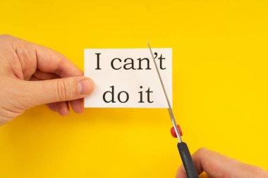 Dişi eller, içinde yazamayacağım bir kağıt ve sarı bir arka planda makas tutuyor.