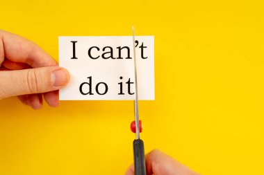 Dişi eller, içinde yazamayacağım bir kağıt ve sarı bir arka planda makas tutuyor.