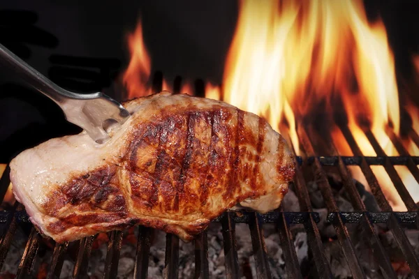 Bife de lombo de porco na grelha de churrasco em chamas quente com garfo — Fotografia de Stock