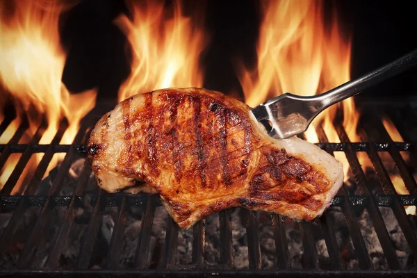 Bife de porco na grelha de churrasco em chamas quente com garfo — Fotografia de Stock
