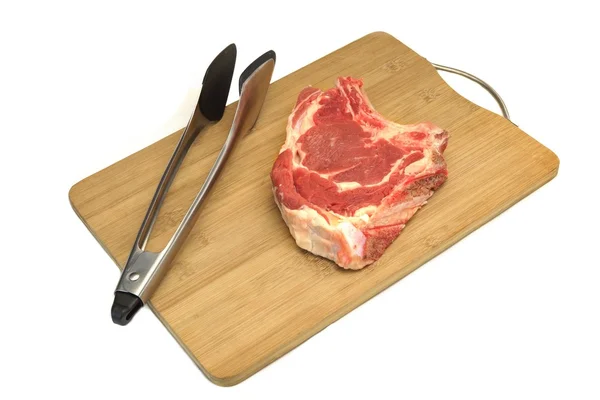 Rå nötkött biff, tång på trä skärbräda isolerade — Stockfoto