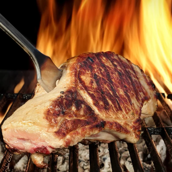 Bife de lombo de porco na grelha de churrasco em chamas quente com garfo — Fotografia de Stock