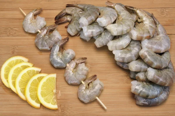 Beaucoup de crevettes crues sur brochette avec du citron sur fond en bois — Photo