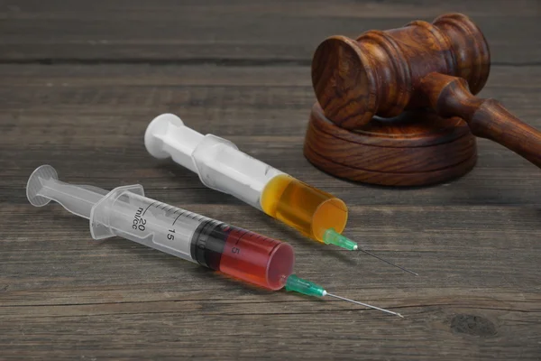 Juízes Gavel e seringas de injeção médica na parte traseira de madeira preta — Fotografia de Stock