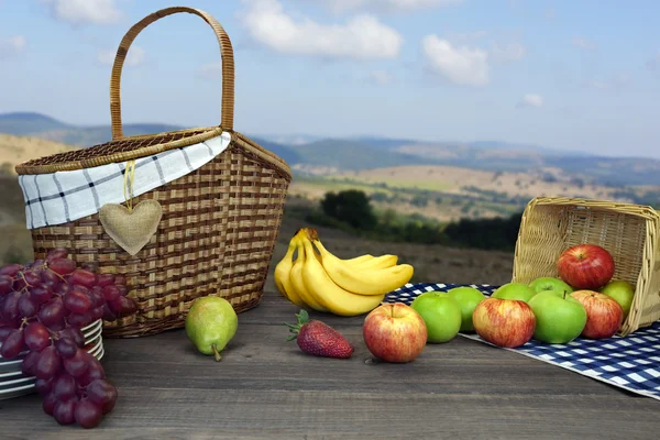 Stół piknikowy z dwoma koszykami i owocami i krajobrazem górskim — Zdjęcie stockowe