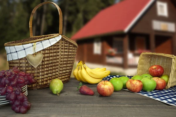 Piknik masa iki sepet ve meyve yakınındaki kır evi — Stok fotoğraf