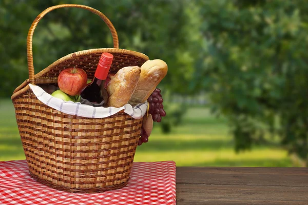 Корзина для пикника с едой и напитками на деревянном столе — стоковое фото