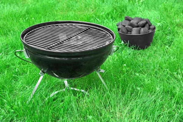 Grelha de churrasco portátil e cesta com Briquetes de carvão no gramado — Fotografia de Stock