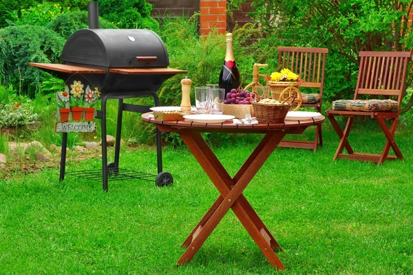 周末在夏季在后院烧烤家庭晚会的现场 木炭烧烤烧烤装置与值得欢迎的迹象和户外木制家具在花园的草坪上 午餐食品和饮料与表 — 图库照片