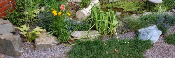 Landscaped Garden Backyard with Designed Landscaping Elements. Garden with Decorative Brick Wall, Small Pond and Tiled Ground from Natural Martials as Mulch, Pebble, Rock and Grass. Designed Garden.