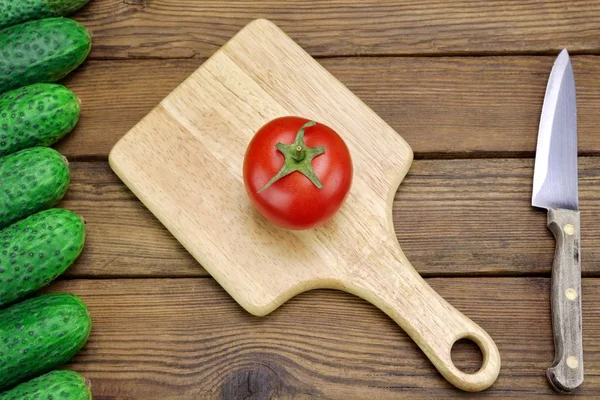 Tomate, pepinos e faca de cozinha no fundo de madeira áspera — Fotografia de Stock