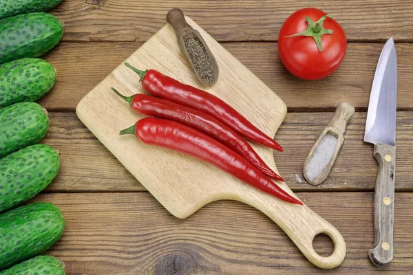 Tomaten, komkommers, mes en hete pepers op de houten achtergrond — Stockfoto