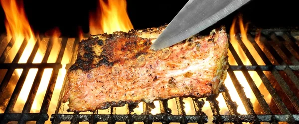 Faca em costelas de porco na churrasqueira em chamas quente — Fotografia de Stock