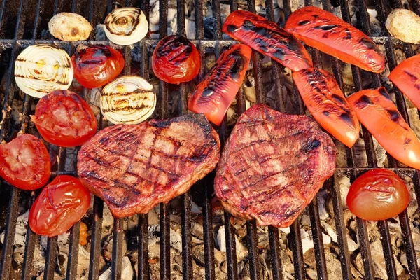 Two Flame Broiled Beef Steaks And Vegetables On BBQ Grill