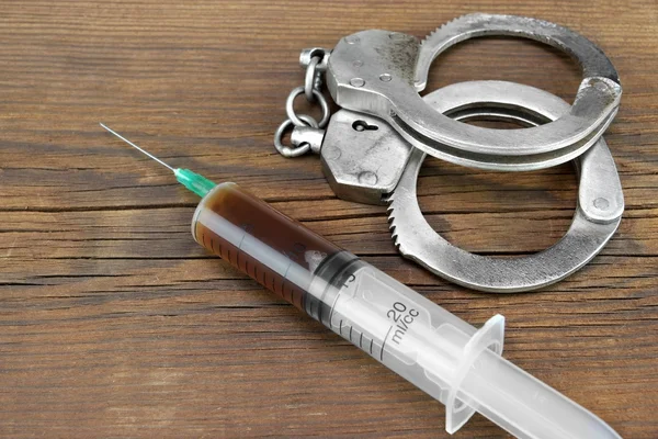 Medical Syringe And Handcuffs On The Wooden Table — Stock Photo, Image