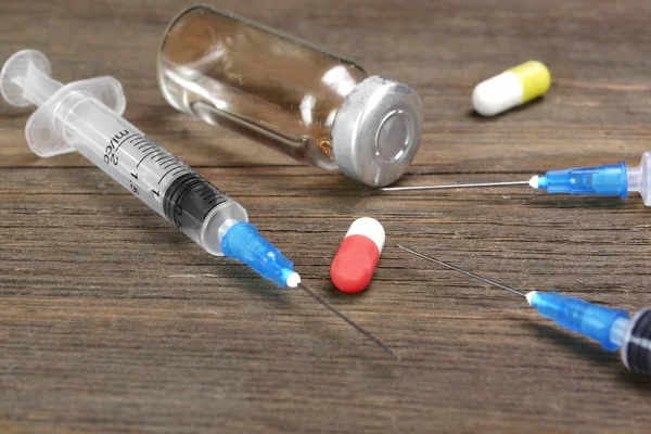 Лекарственные пробирки, шприц и лекарства на деревянном столе — стоковое фото