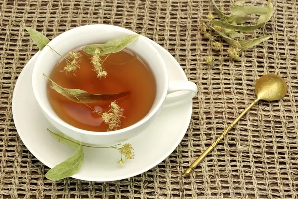Чашка чая с травяным чаем и ложкой на скатерти — стоковое фото