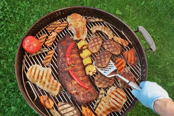 Hand mit Spachtel und Grill mit Fleisch und Gemüse — Stockfoto