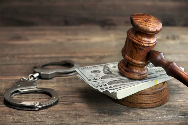 Dollar banknotes, handcuffs and judge gavel on wood table — Stockfoto