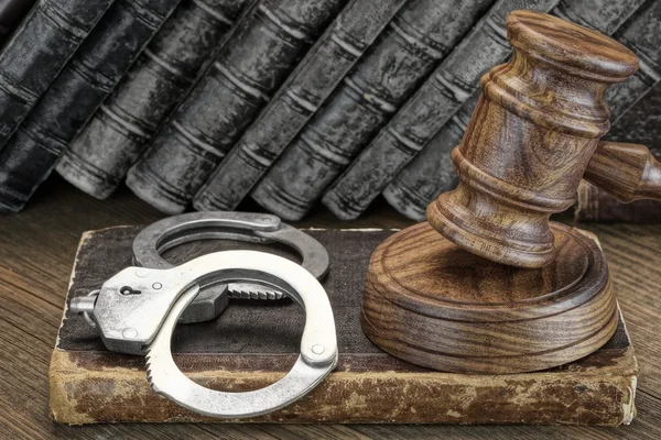 手錠、裁判官小槌と木製のテーブルの古い法律の本 — ストック写真